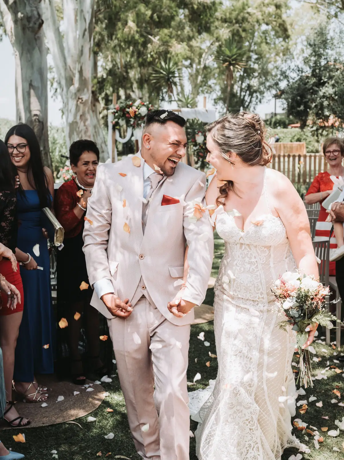 Couple laughing under falling petals at their wedding exit — candid documentary wedding photography in Spain