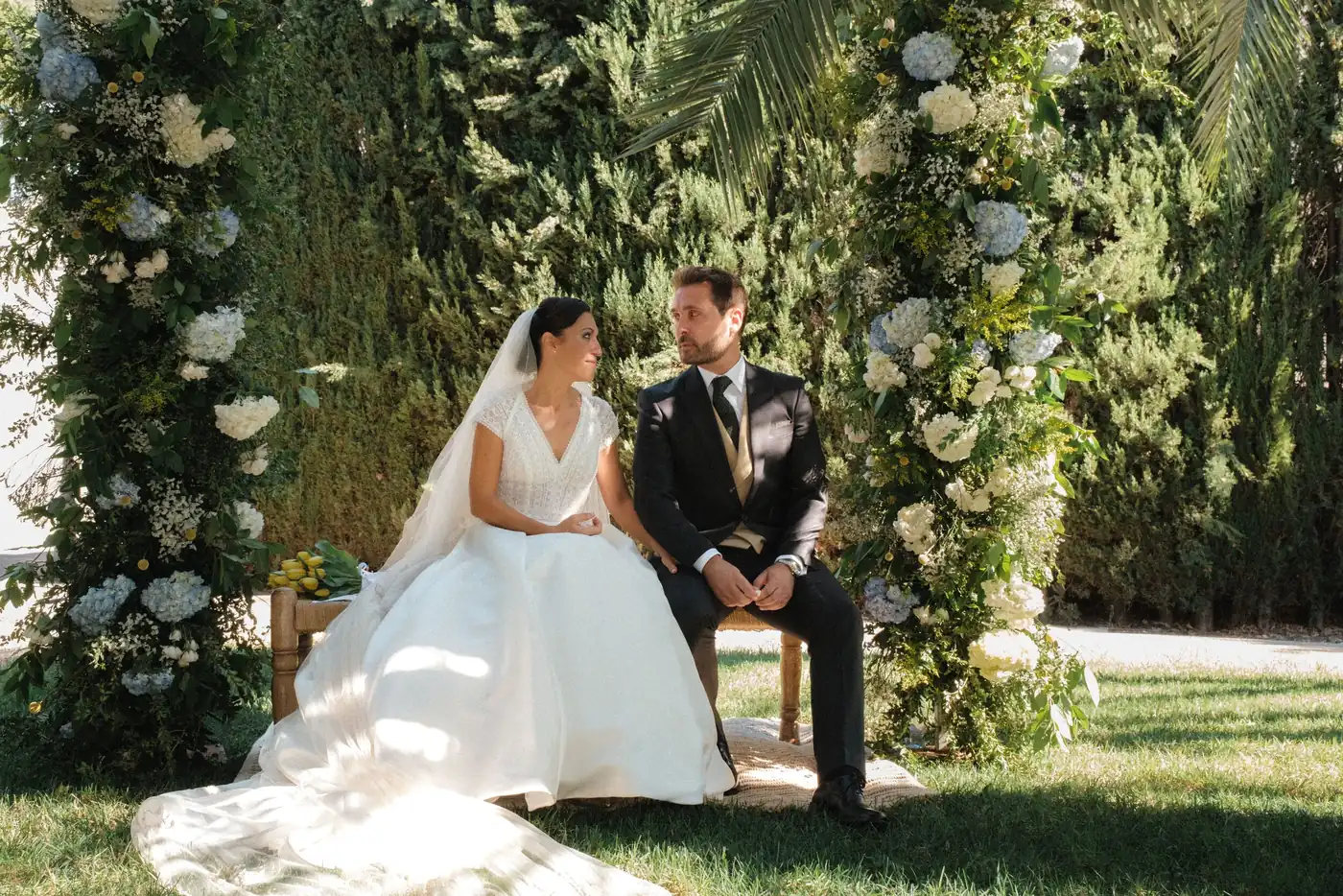 Fotógrafo de bodas en Barcelona — pareja bajo un arco floral en un jardín mediterráneo por iArtist Studios